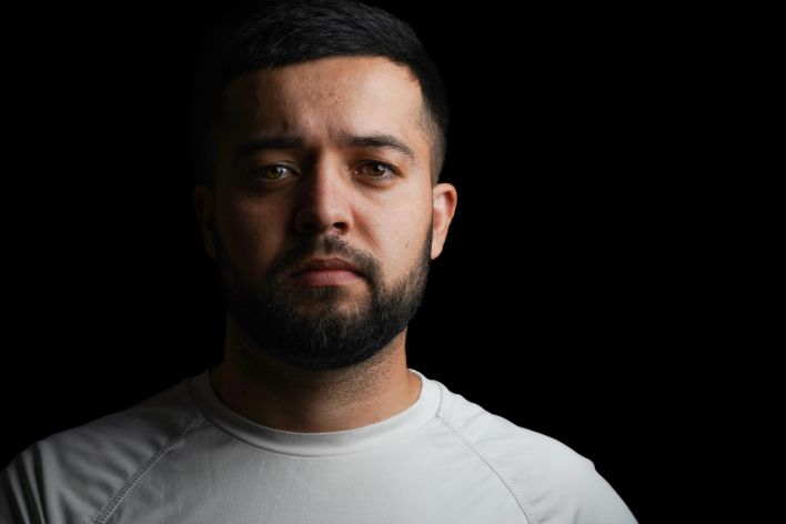 Studio portrait of a serious man with a beard in a white t-shirt against a black backdrop.