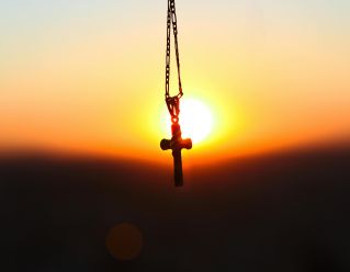 A cross pendant silhouetted against a vibrant sunset, symbolizing faith and peace.
